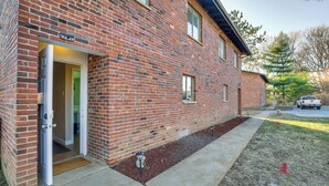 Un bâtiment en briques avec une porte ouverte, une petite fenêtre et un véhicule garé à l’arrière-plan.