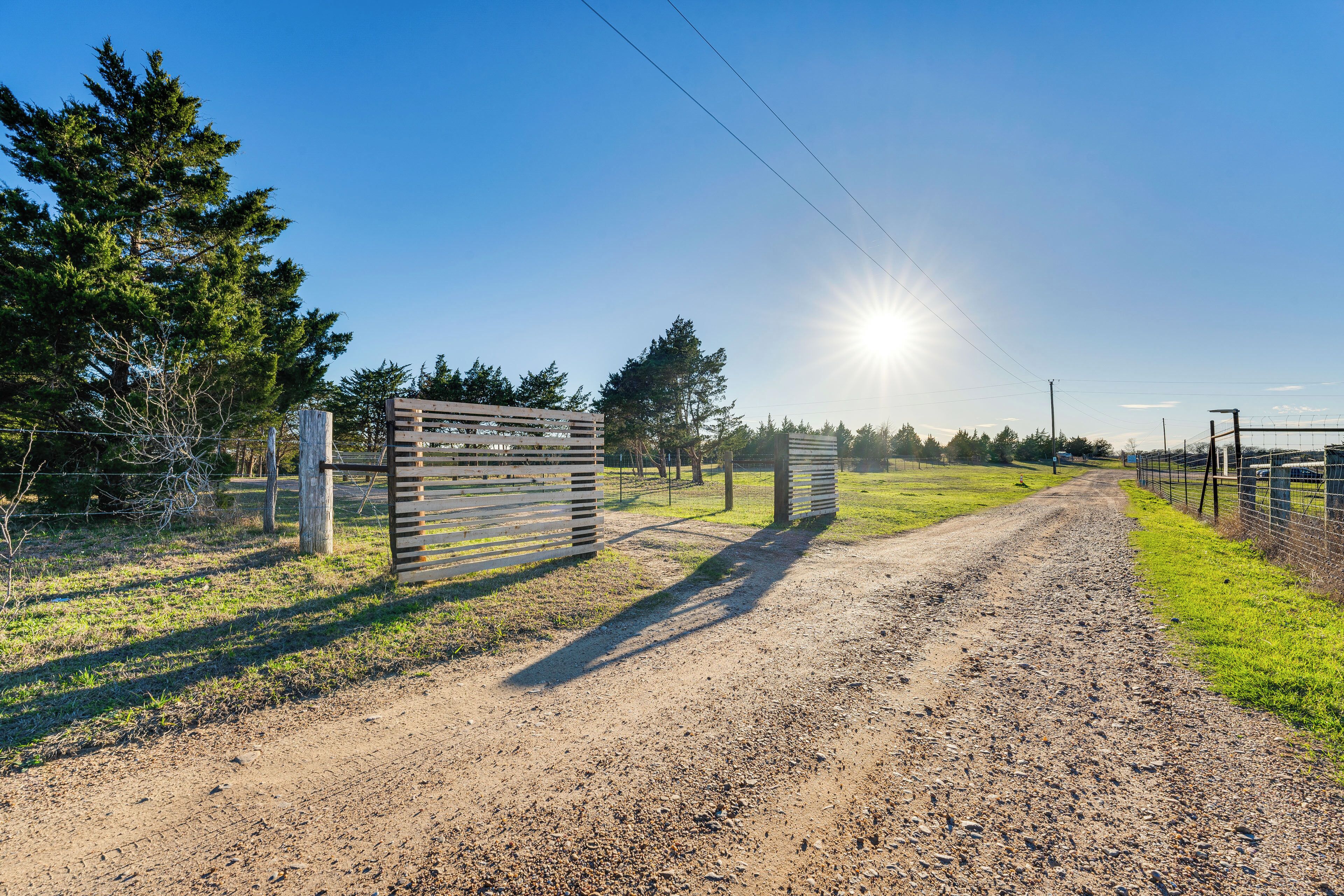 A gravel path leading to a gated area with a fence, surrounded by trees and open fields.