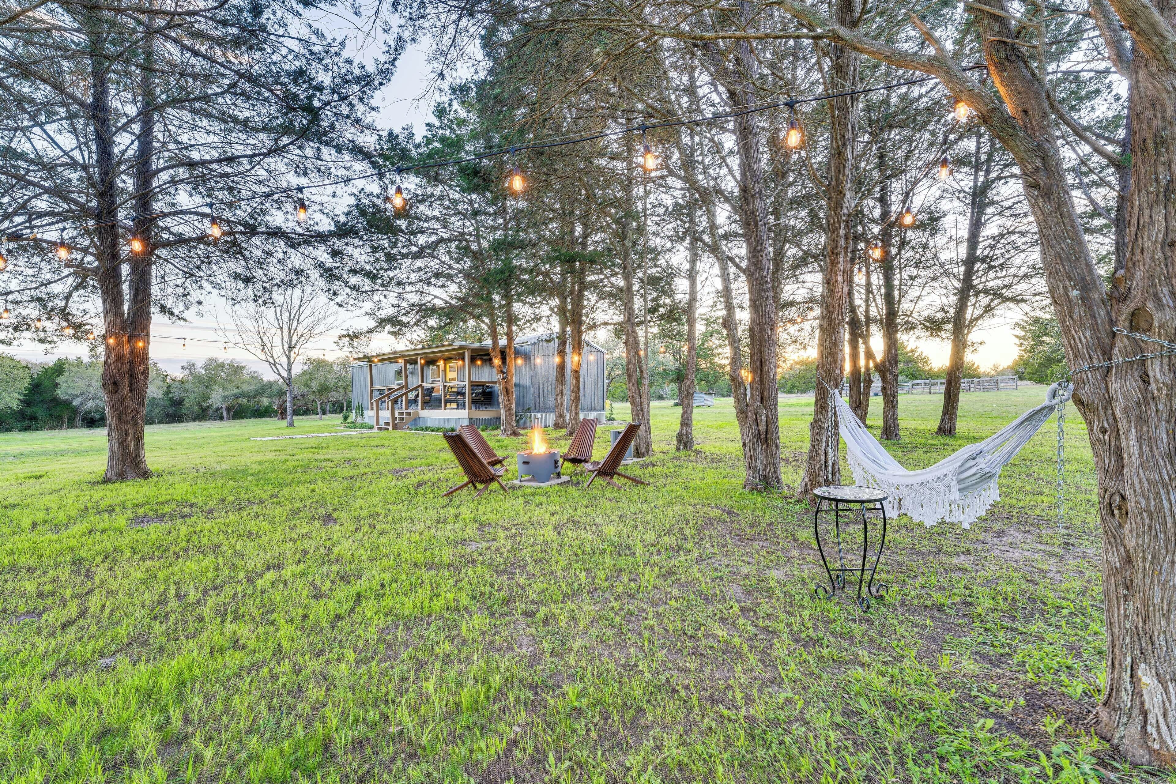 A rustic cabin with a fire pit and seating area surrounded by trees and string lights.
