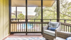 A covered balcony with a wicker sofa, a view of a building, and a pool in the background. - Walk to Ocean: Unit w/ 2 Balconies in Myrtle Beach (Myrtle Beach)