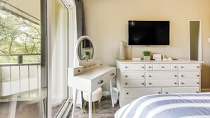 A bedroom with a white dresser, a vanity with a mirror, a flat-screen TV mounted above the dresser, and a bed with striped bedding. - Walk to Ocean: Unit w/ 2 Balconies in Myrtle Beach (Myrtle Beach)