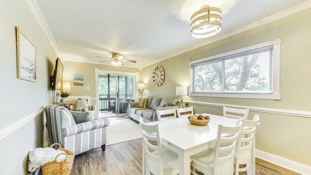 A dining area with a white table and chairs, a ceiling fan, and a window with blinds. - Walk to Ocean: Unit w/ 2 Balconies in Myrtle Beach (Myrtle Beach)