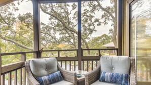 A covered outdoor seating area with wicker chairs and cushions, overlooking a garden and buildings. - Walk to Ocean: Unit w/ 2 Balconies in Myrtle Beach (Myrtle Beach)