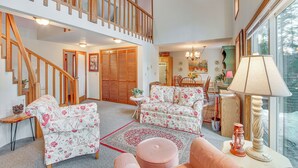 A spacious living room with a staircase, floral-patterned sofas, a dining area, and a large window. - Washington Mountain Cabin: 1 Mi to Lake Cle Elum (Cle Elum)