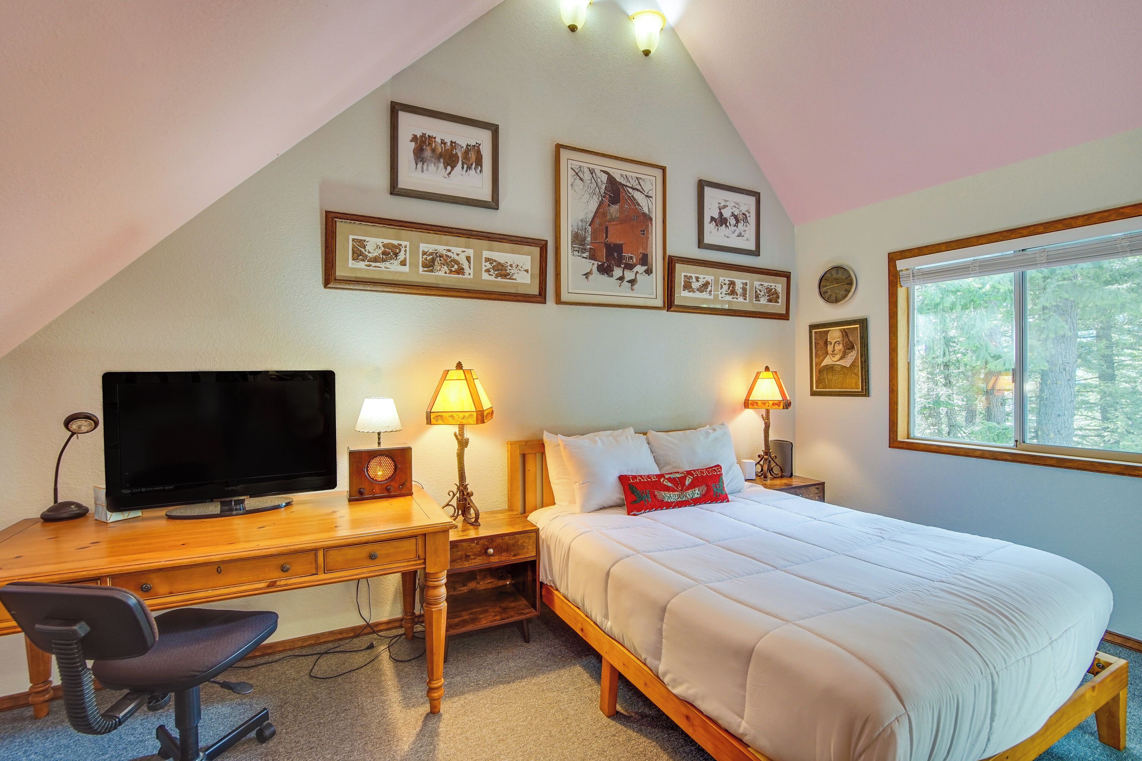 A bedroom with a wooden desk, a bed with white bedding, a television, and framed pictures on the wall.
