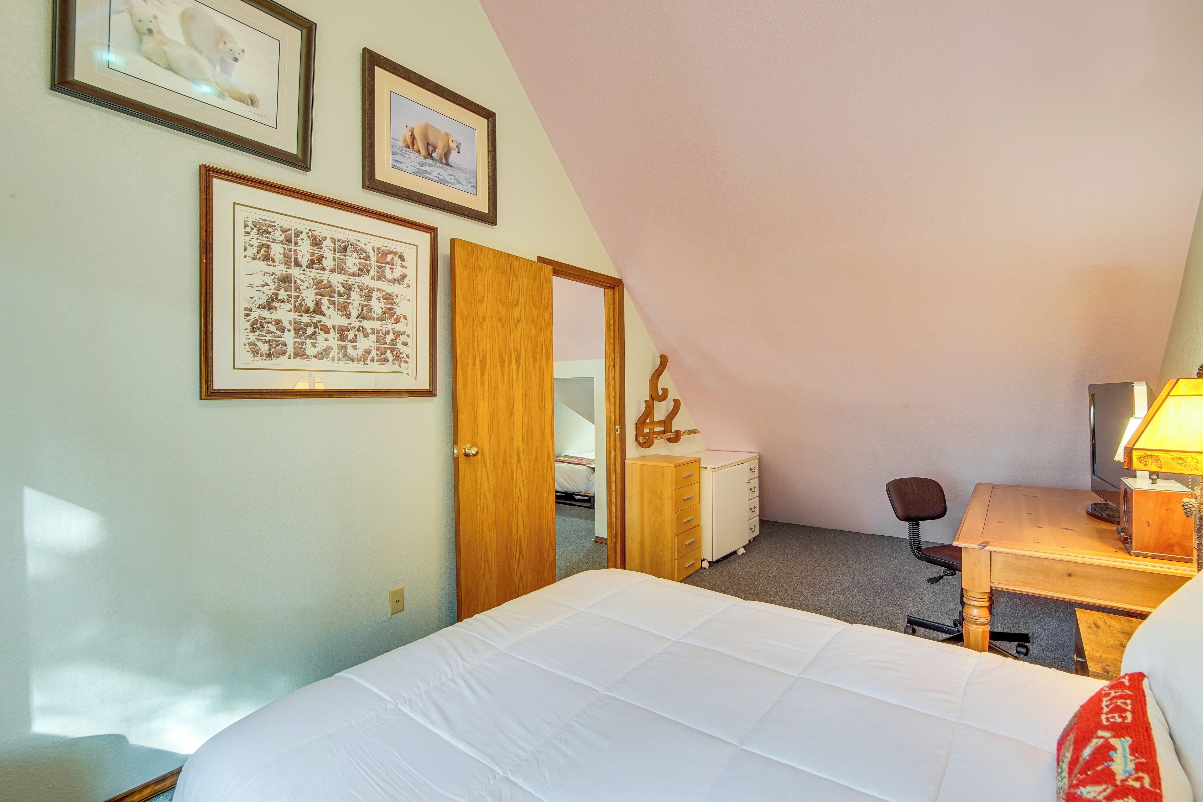 Een slaapkamer met een bed, een bureau, een stoel, een dressoir en ingelijste foto's aan de muur.