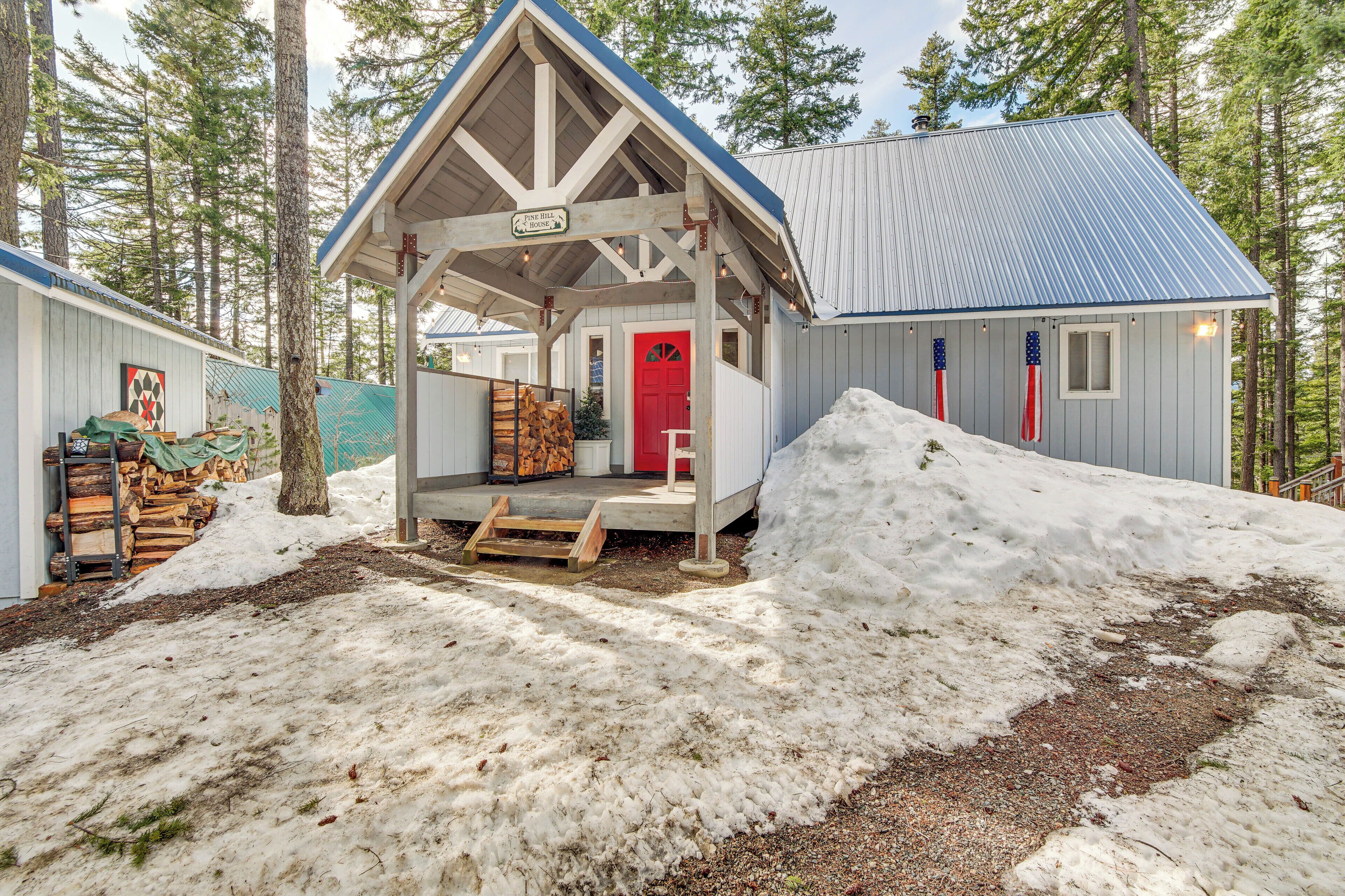 A lodge with a red door and a covered porch, surrounded by snow and trees.