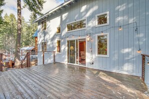 Eine Holzterrasse führt zu einem Haus mit vielen Fenstern und einer Tür, umgeben von Bäumen.