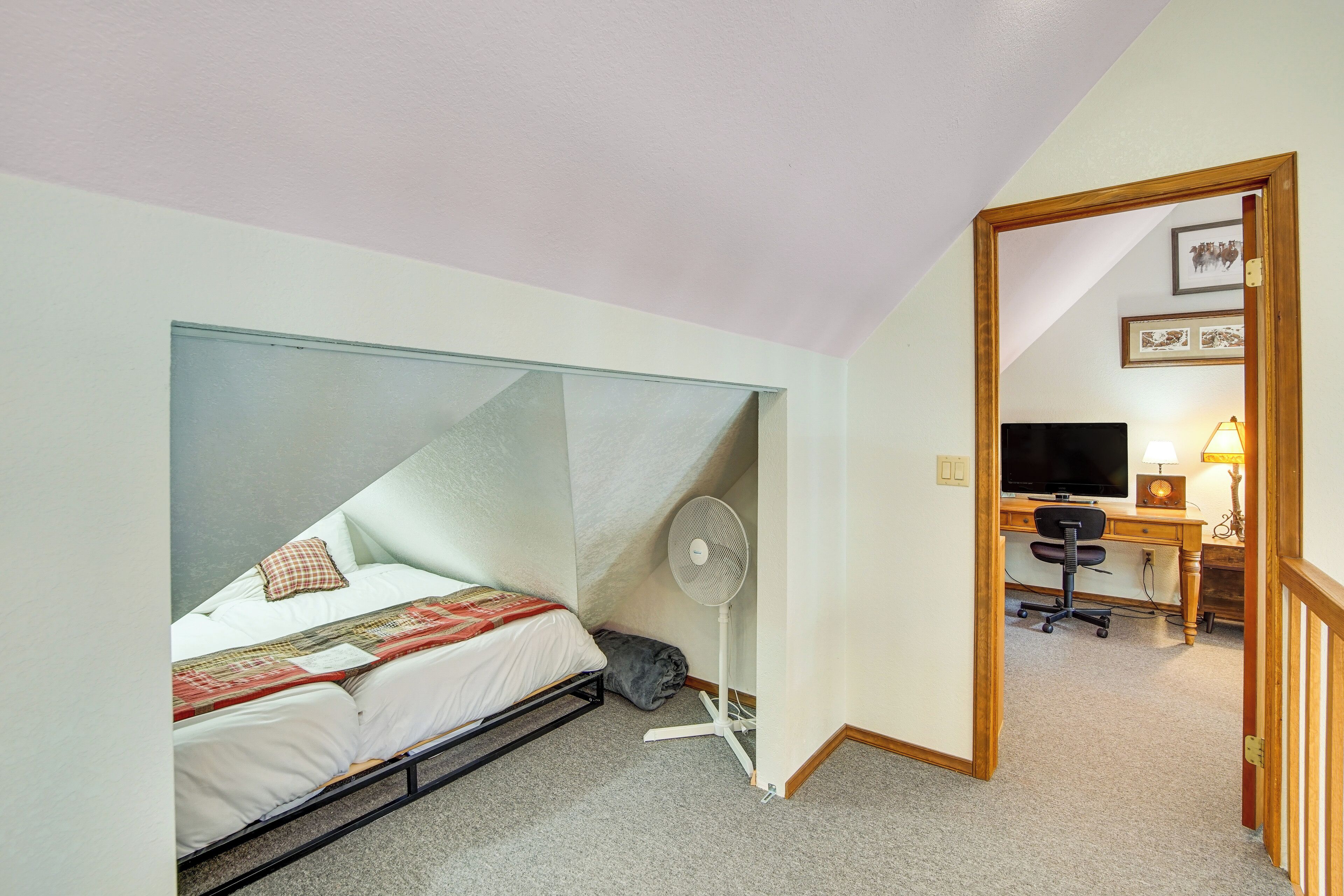 Un dormitorio con cama, ventilador, escritorio con silla y televisor.