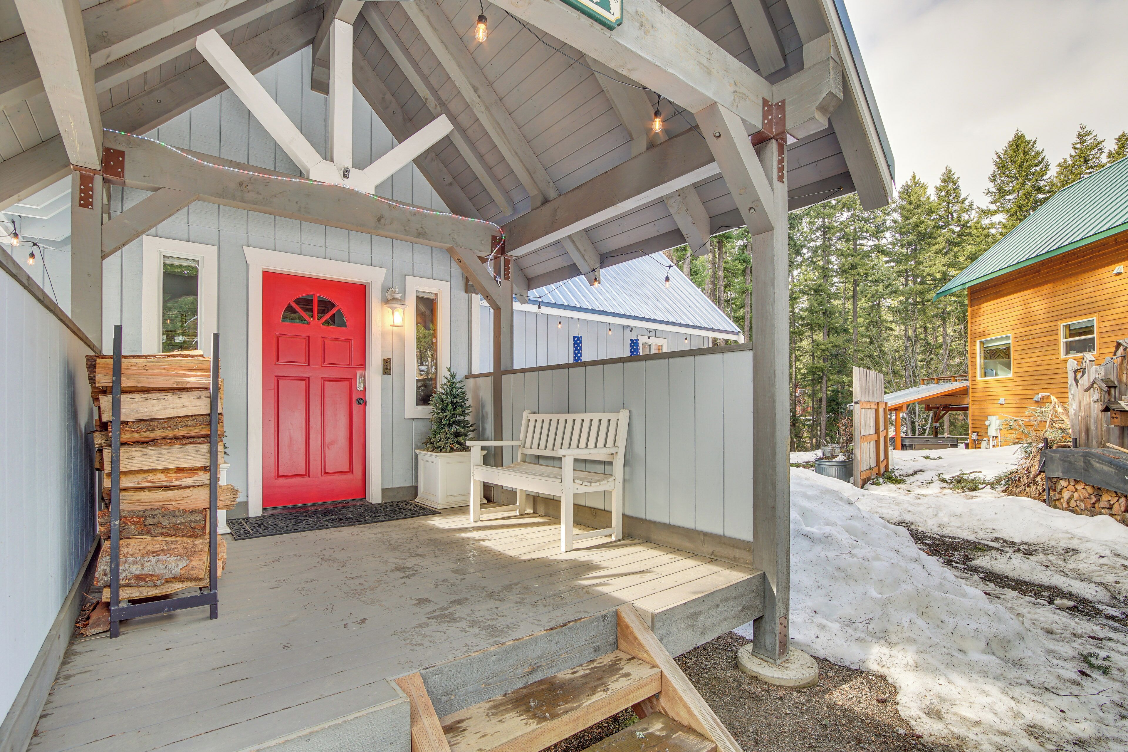 A covered porch with a red door, wooden benches, and a stack of firewood.