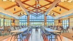 Un amplio comedor interior con techos altos y luz natural proveniente de grandes ventanales. Mesas y sillas dispuestas para comidas grupales.