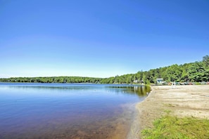 A serene lakeside view with a clear sky, calm water, and a forested shoreline.