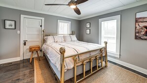 A bedroom with a bed, a ceiling fan, a door, and windows. - Peaceful Cottage w/ Yard: 2 Mi to Kentucky Lake! (Stewart)