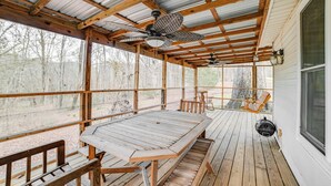 A covered outdoor deck with a wooden table and benches, metal mesh fencing, and a view of trees. - Peaceful Cottage w/ Yard: 2 Mi to Kentucky Lake! (Stewart)