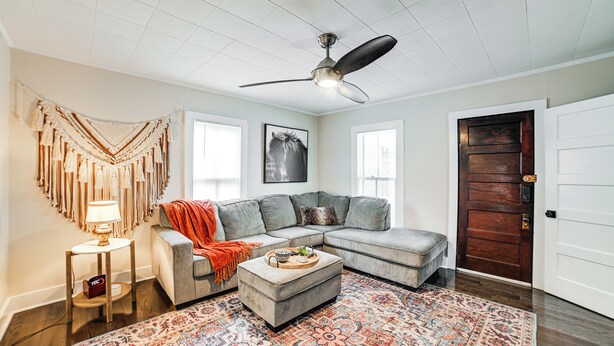 A living room with a sectional sofa, a ceiling fan, a patterned rug, and a wooden door. - Peaceful Cottage w/ Yard: 2 Mi to Kentucky Lake! (Stewart)