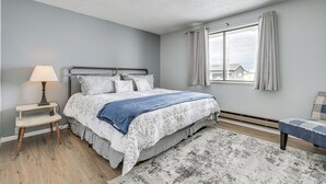 A bedroom with a bed, bedside table, lamp, and a view of the outside. - Dog-friendly Montana Home w/ Deck & Fenced-in Yard (Dillon)