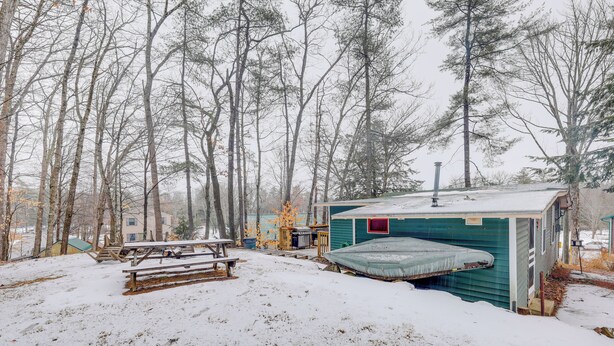 Une cabane dotée d’un petit porche et d’un espace abrité, entourée d’arbres et de neige.