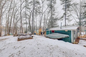A cabin with a small porch and a covered area, surrounded by trees and snow. - Lovely Maine Cabin w/ Deck, Gas Grill & Fire Pit! (Casco)