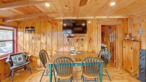 Un intérieur en bois comprenant une table à manger, quatre chaises, un ventilateur de plafond et un téléviseur.
