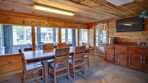 A wooden interior with a dining table and chairs, a kitchen area with cabinets and a sink, and large windows offering views of the outdoors. - Charming Home w/ Dock, Near Downtown Lake Charles! (Lake Charles)