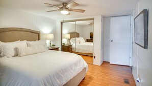 A bedroom with a large bed, a ceiling fan, a mirror, and a door. - Charming Home w/ Dock, Near Downtown Lake Charles! (Lake Charles)