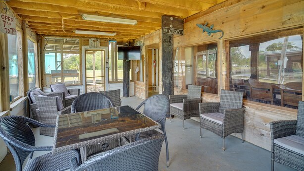 An indoor seating area with wicker furniture and a glass table, wooden ceiling, and large windows. - Charming Home w/ Dock, Near Downtown Lake Charles! (Lake Charles)