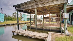 A wooden dock extending into a calm body of water, with a covered wooden structure in the background. - Charming Home w/ Dock, Near Downtown Lake Charles! (Lake Charles)