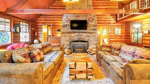 A log cabin interior with a stone fireplace, wooden furniture, and a television mounted above it. - Forested 'minikahda Lodge' w/ Hot Tub Near Mt Hood (Rhododendron)