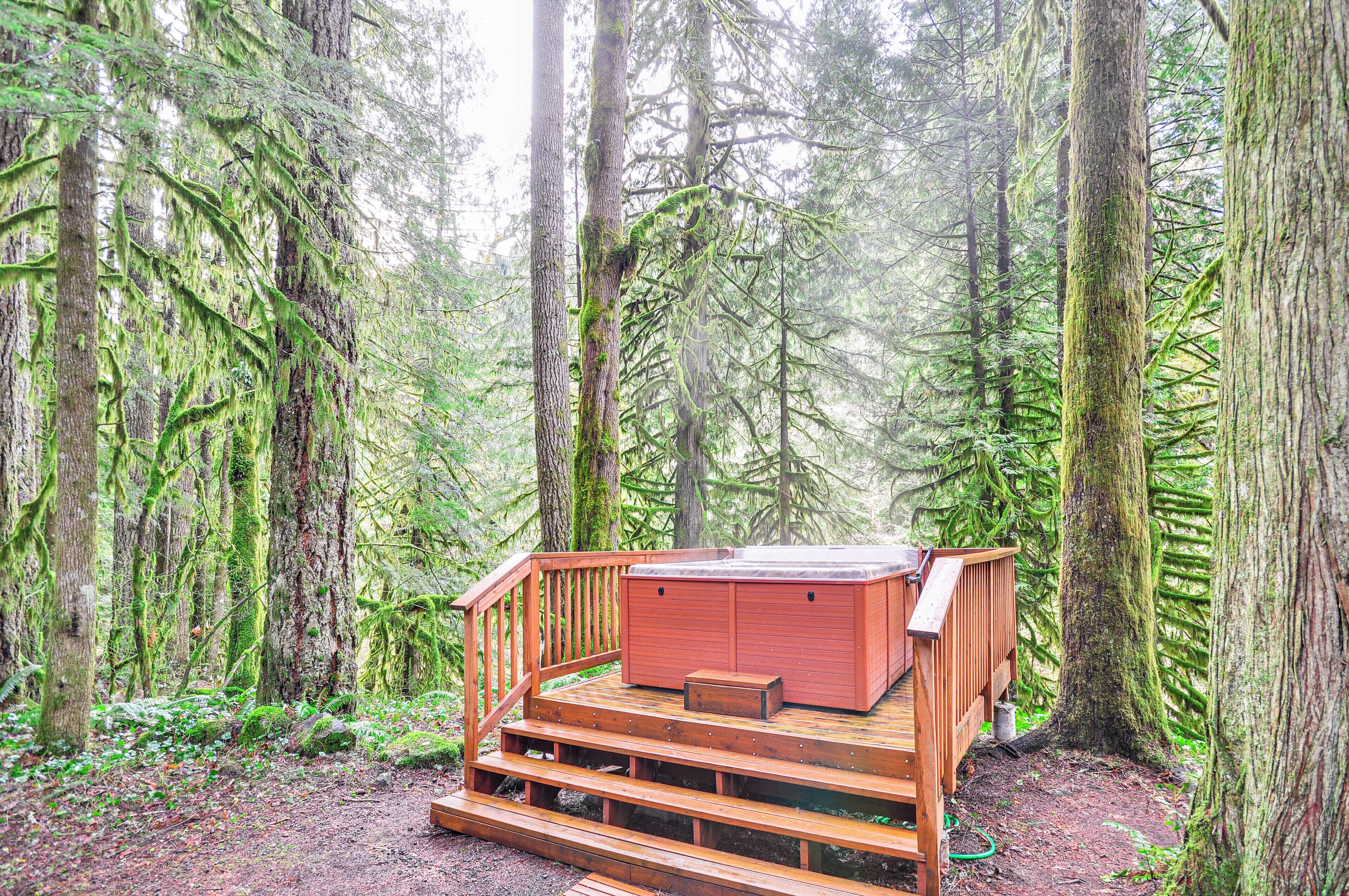 A wooden deck with a hot tub and a small seating area surrounded by a forest.