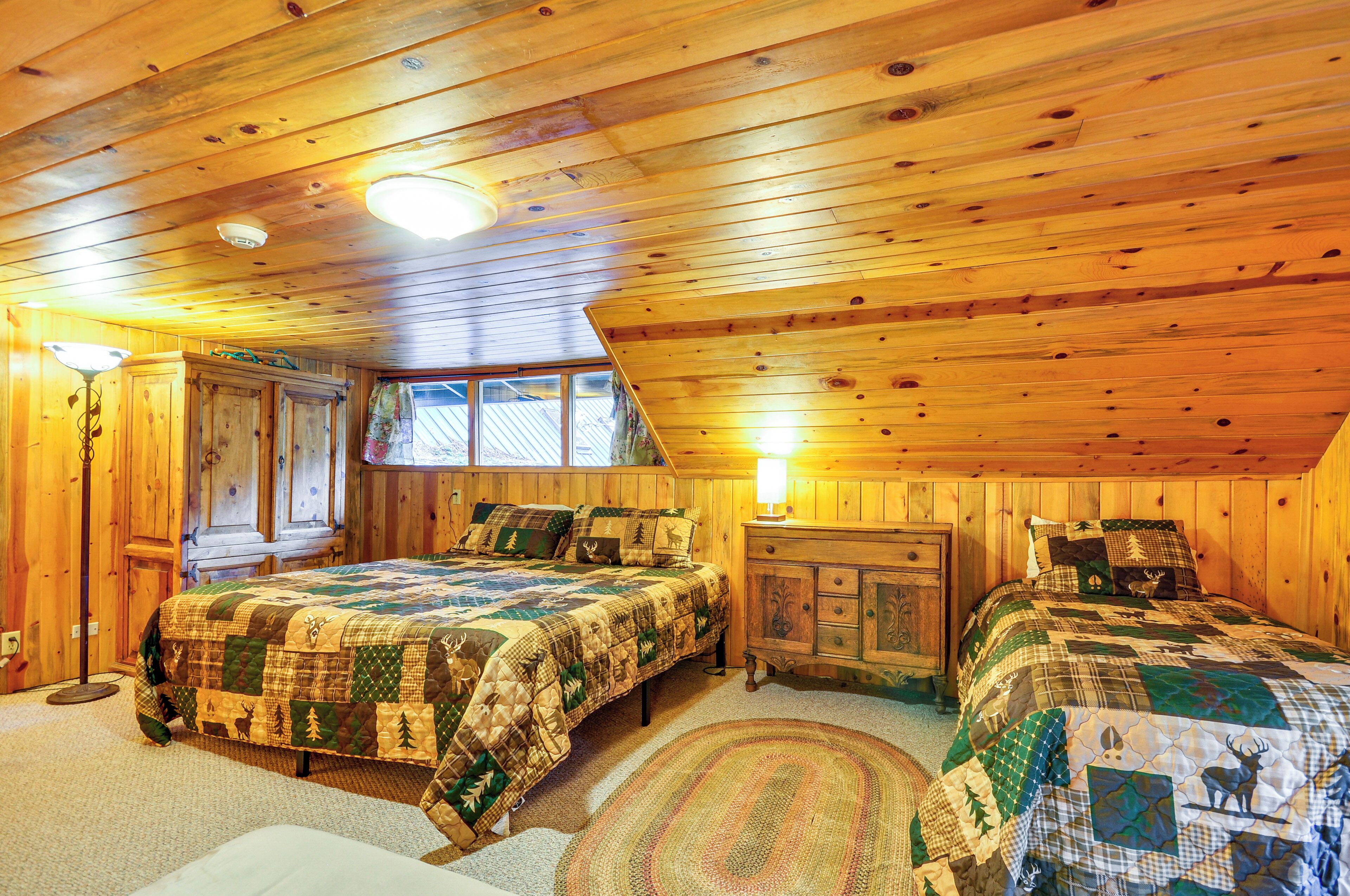 A cozy cabin-style bedroom with two beds, a wooden ceiling, and a large window.