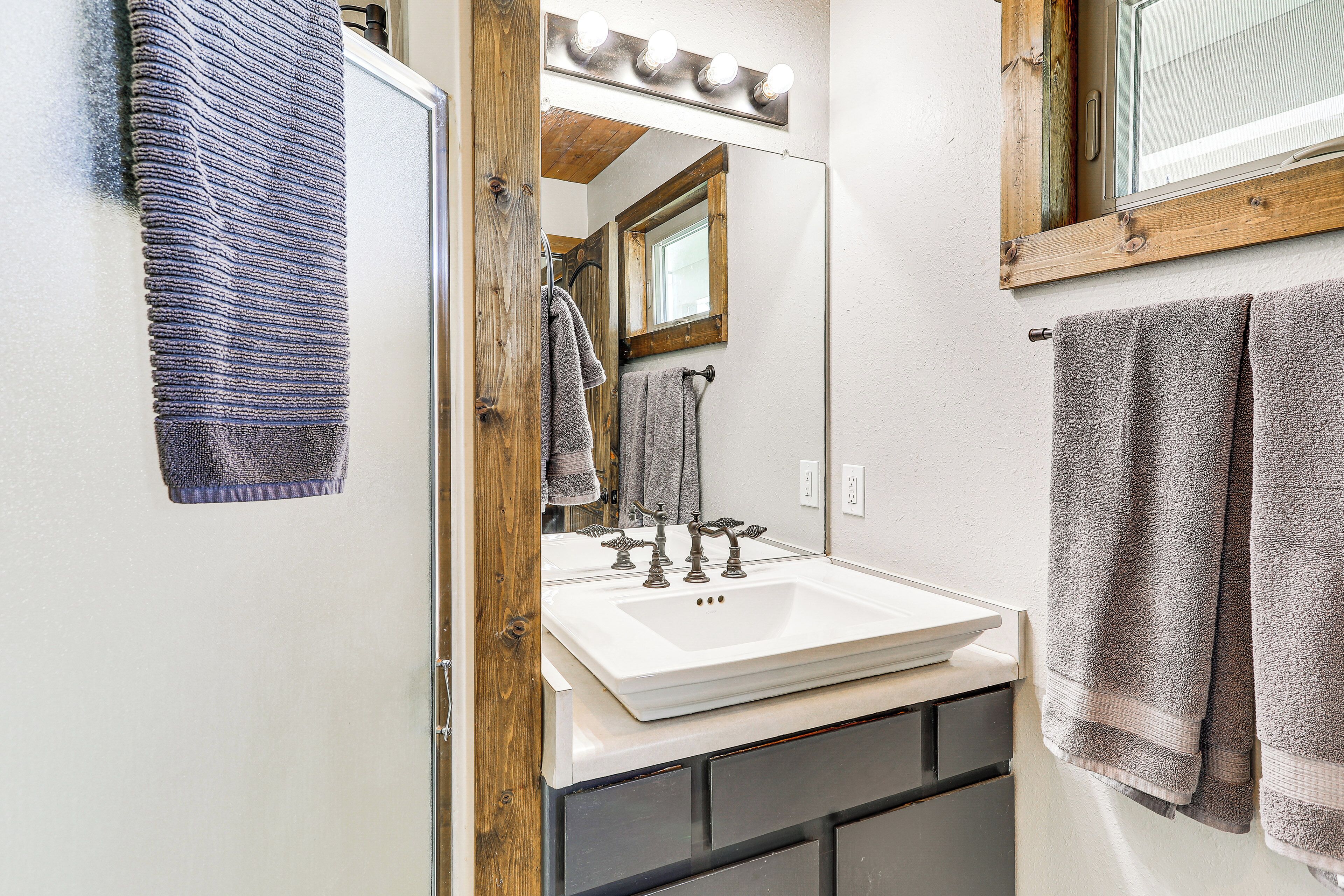A bathroom with a white sink, wooden vanity, and a mirror with lights above it.