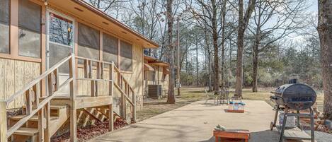 A wooden cabin with a deck, a barbecue grill, and a concrete patio.