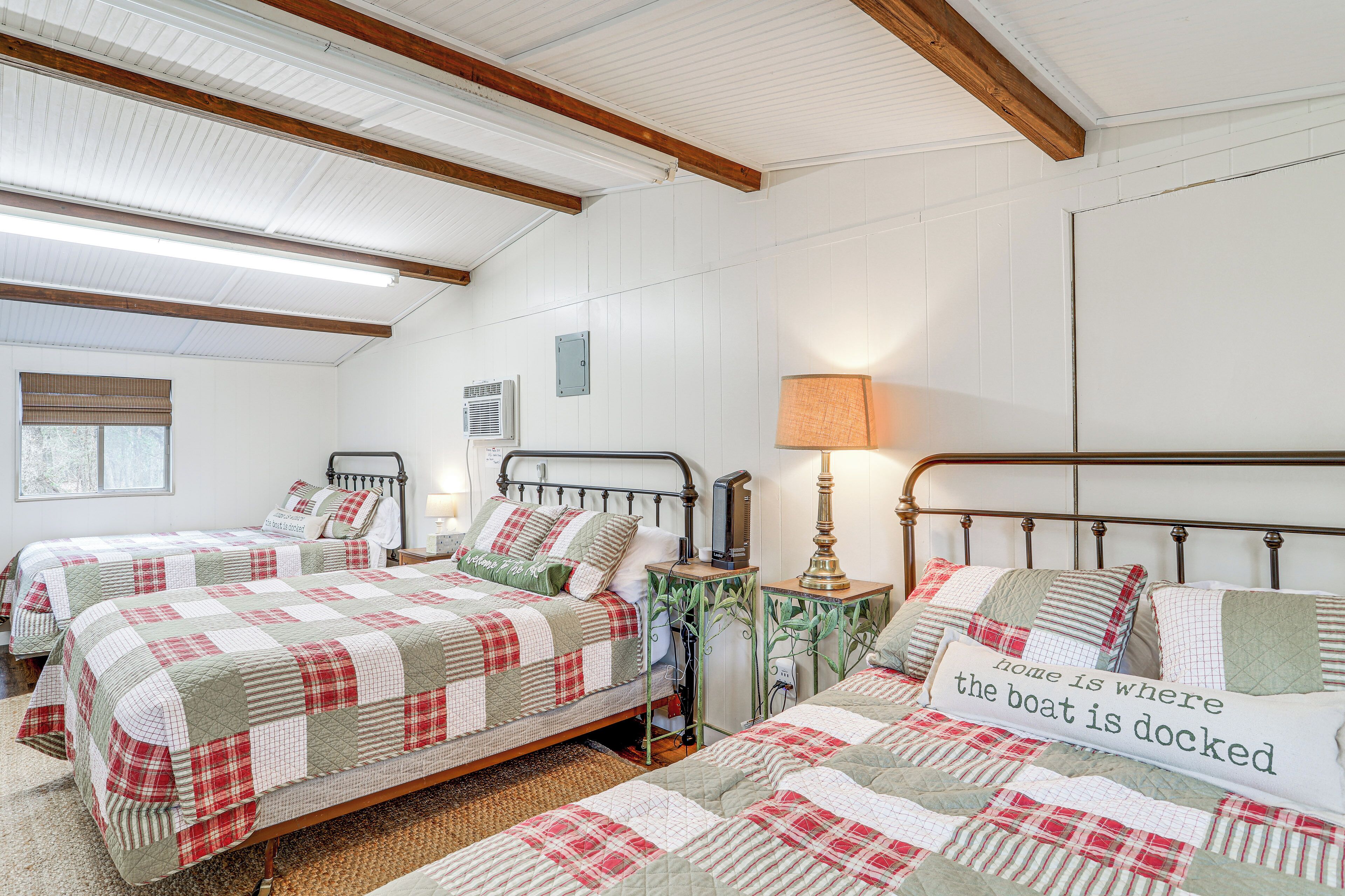 A bedroom with two beds, a bedside table, a lamp, and a window with blinds.