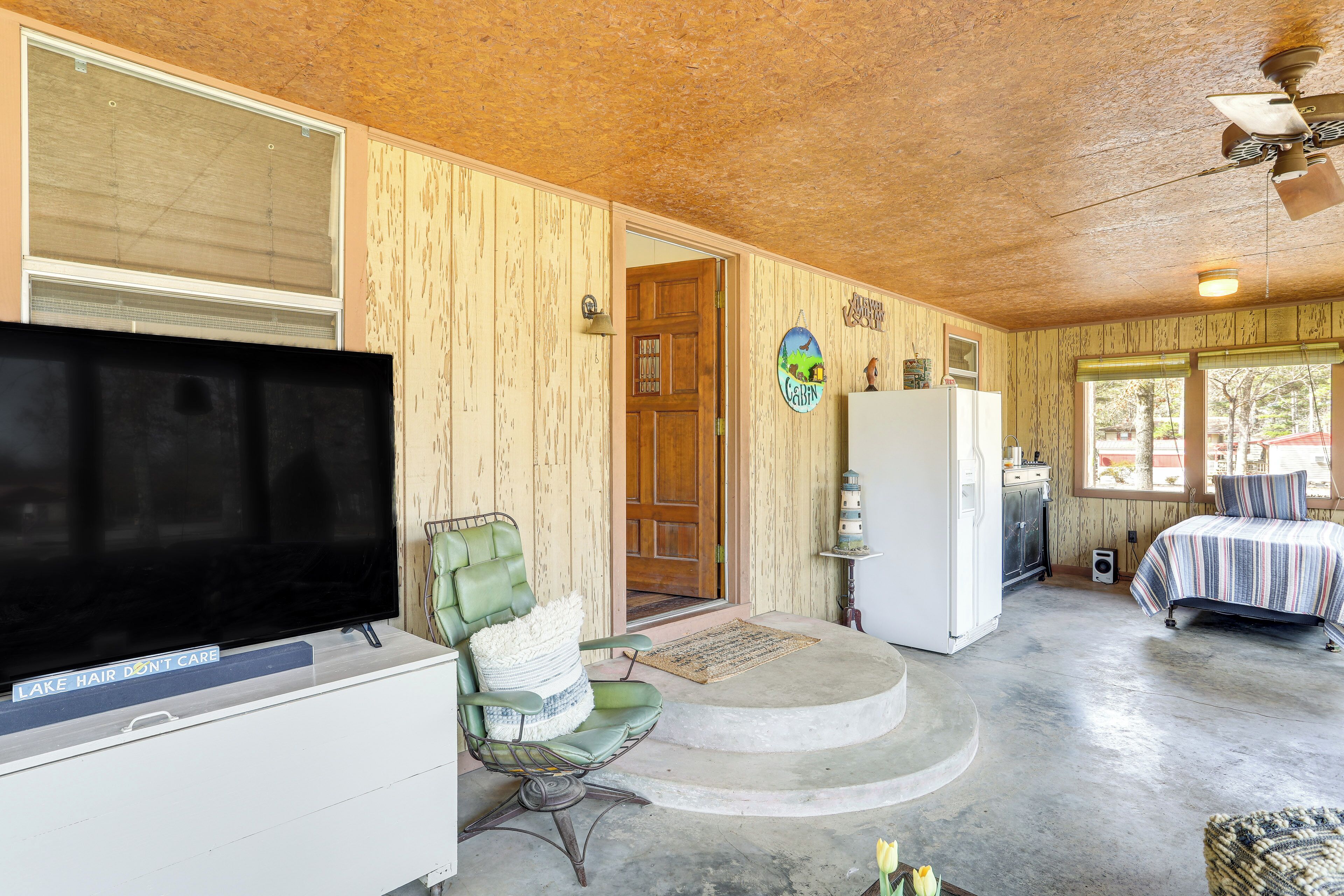 A room with a television, a green chair, a bed, a refrigerator, and a wooden ceiling.