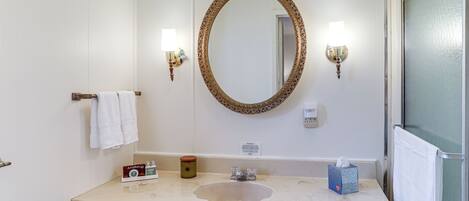 Un baño con lavamanos, tocador y un espejo grande con marco decorativo. Hay dos luces fijadas a la pared y un perchero con una toalla blanca.