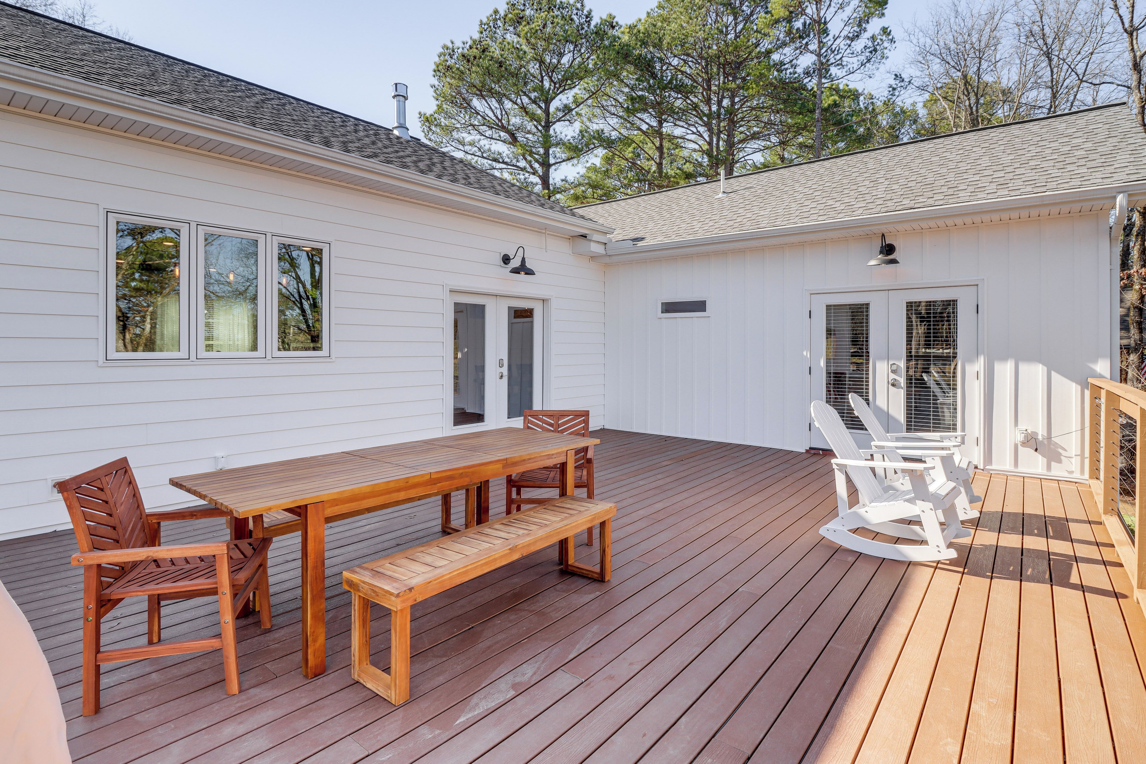 A wooden deck with a table and chairs, a bench, and a rocking chair.
