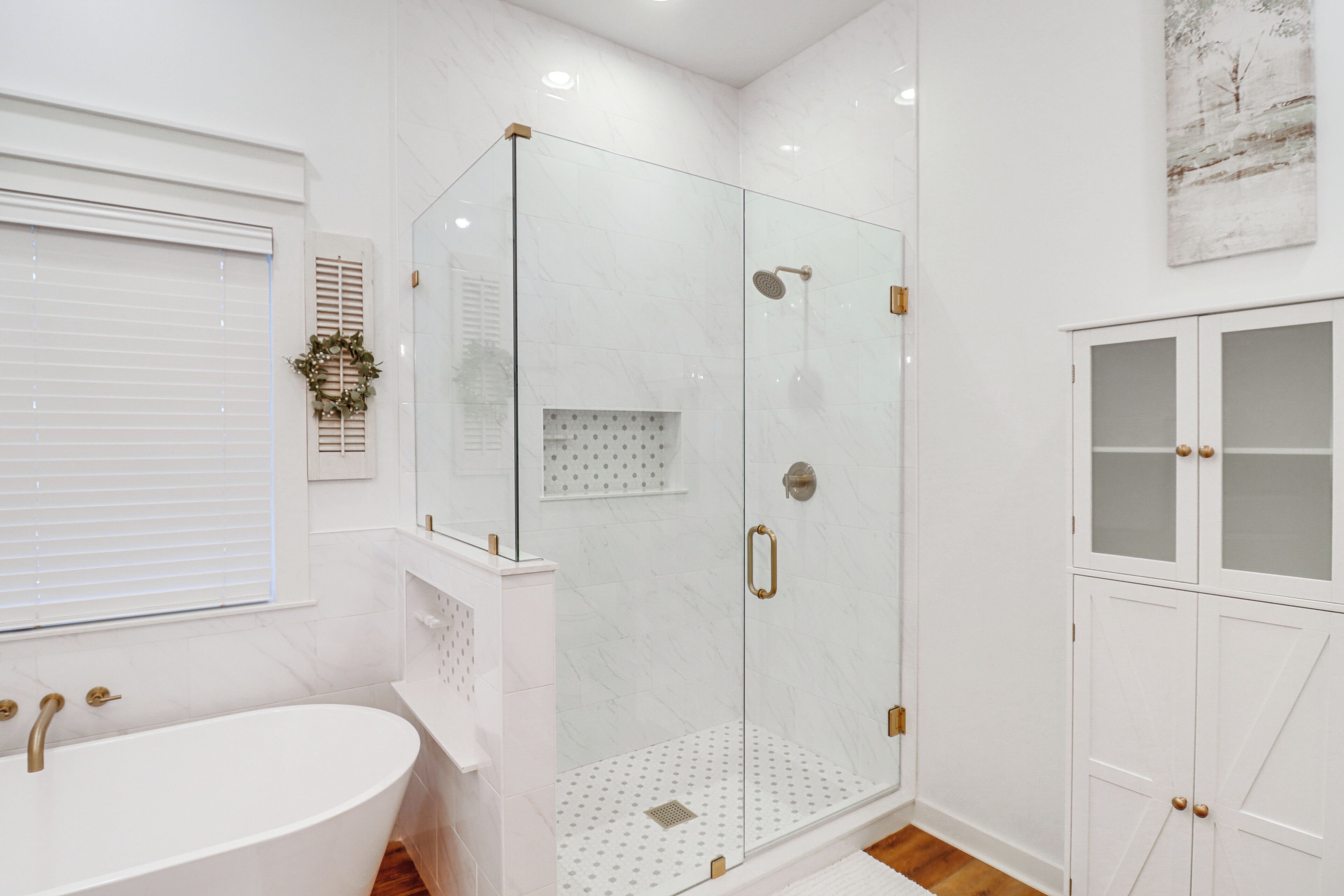 Un baño moderno con una bañera independiente, una ducha con cerramiento de vidrio y un mueble blanco con puertas de cristal.