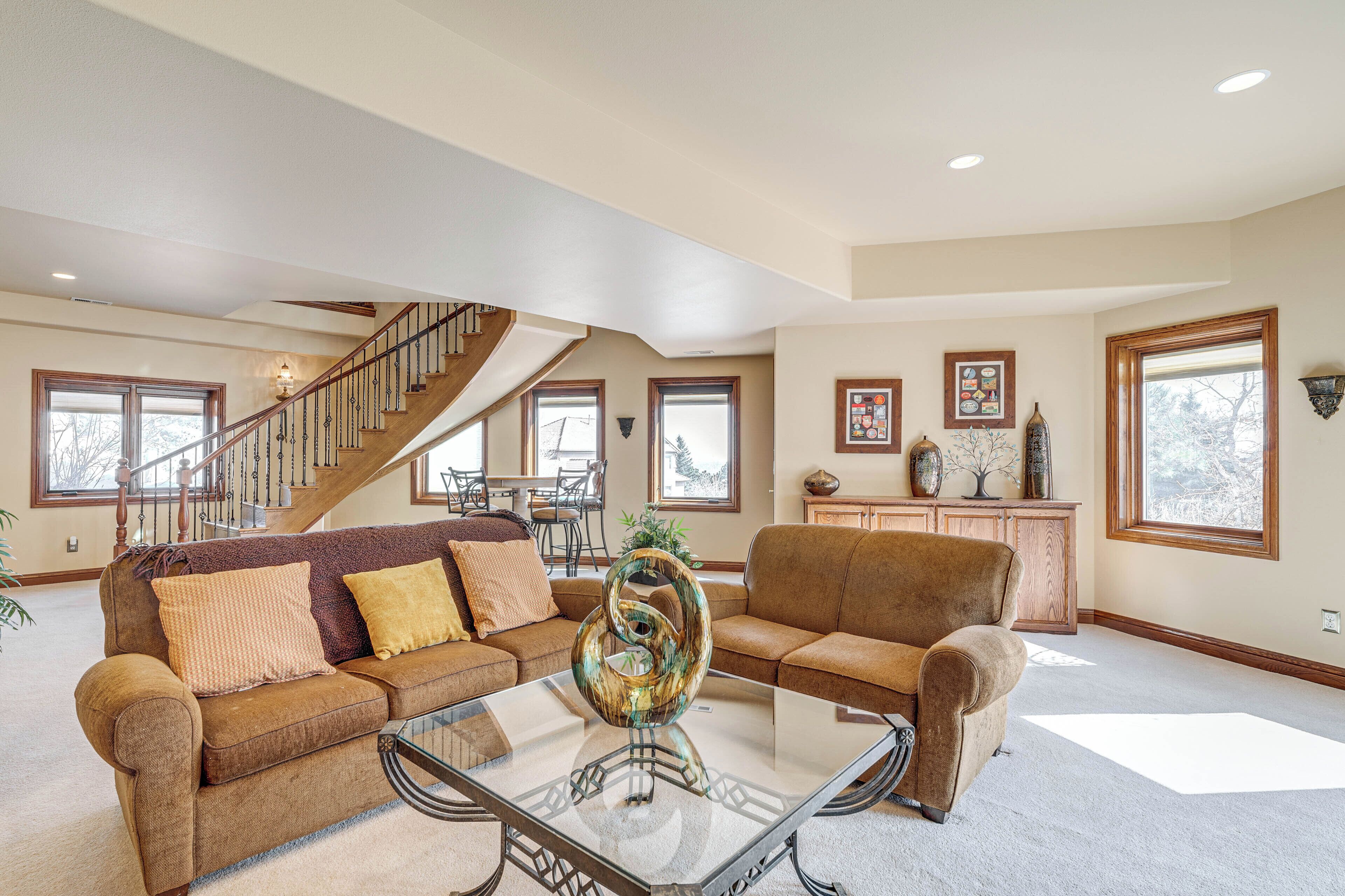 A spacious living room with a glass coffee table, two sofas, a staircase, and large windows.