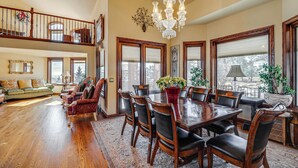 A spacious dining area with a large wooden table and chairs, a chandelier, and large windows with blinds. - Colorado Springs Home ~ 4 Mi to Garden of the Gods (Colorado Springs)