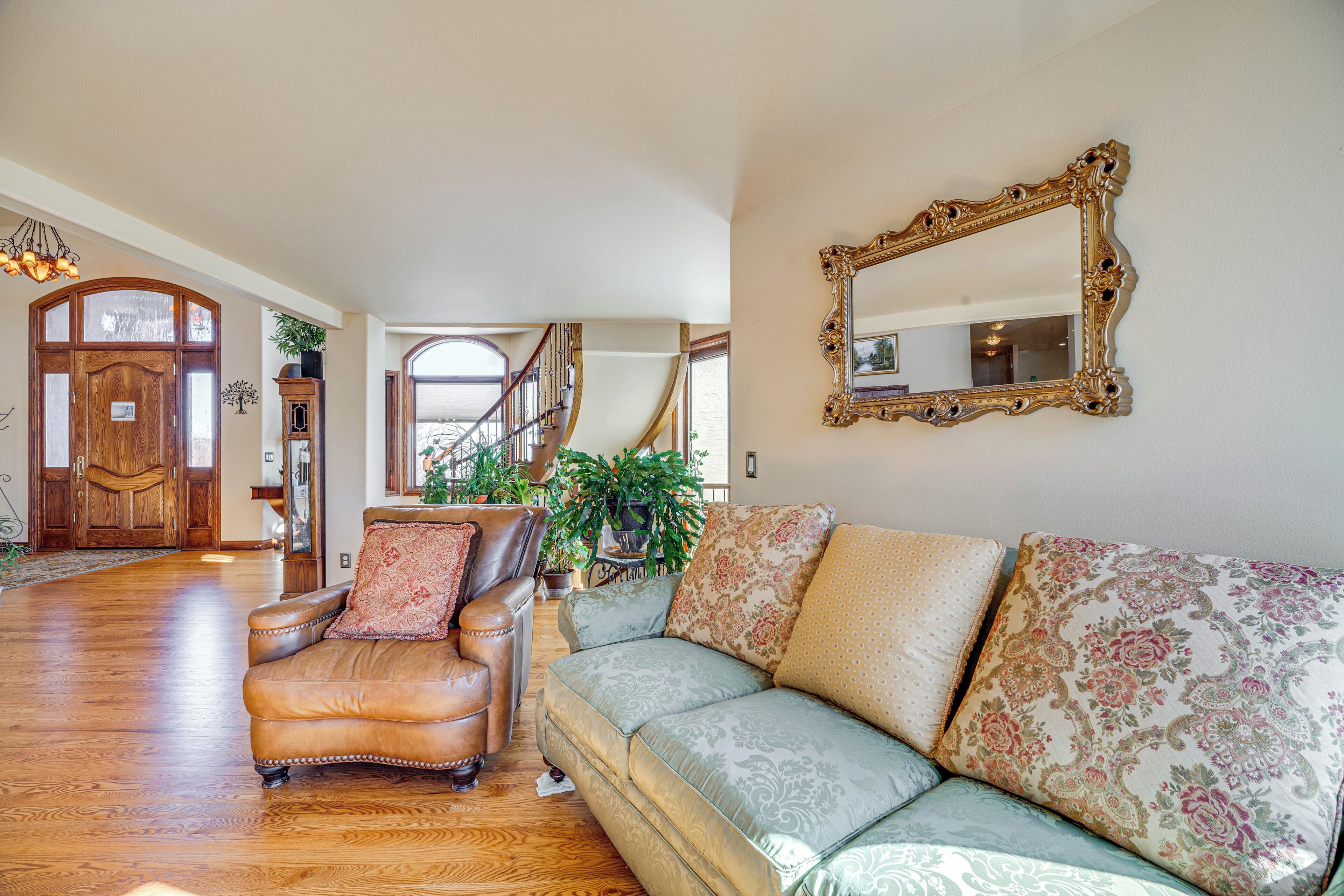 A spacious living room with a leather armchair, a patterned sofa, and a large mirror on the wall.
