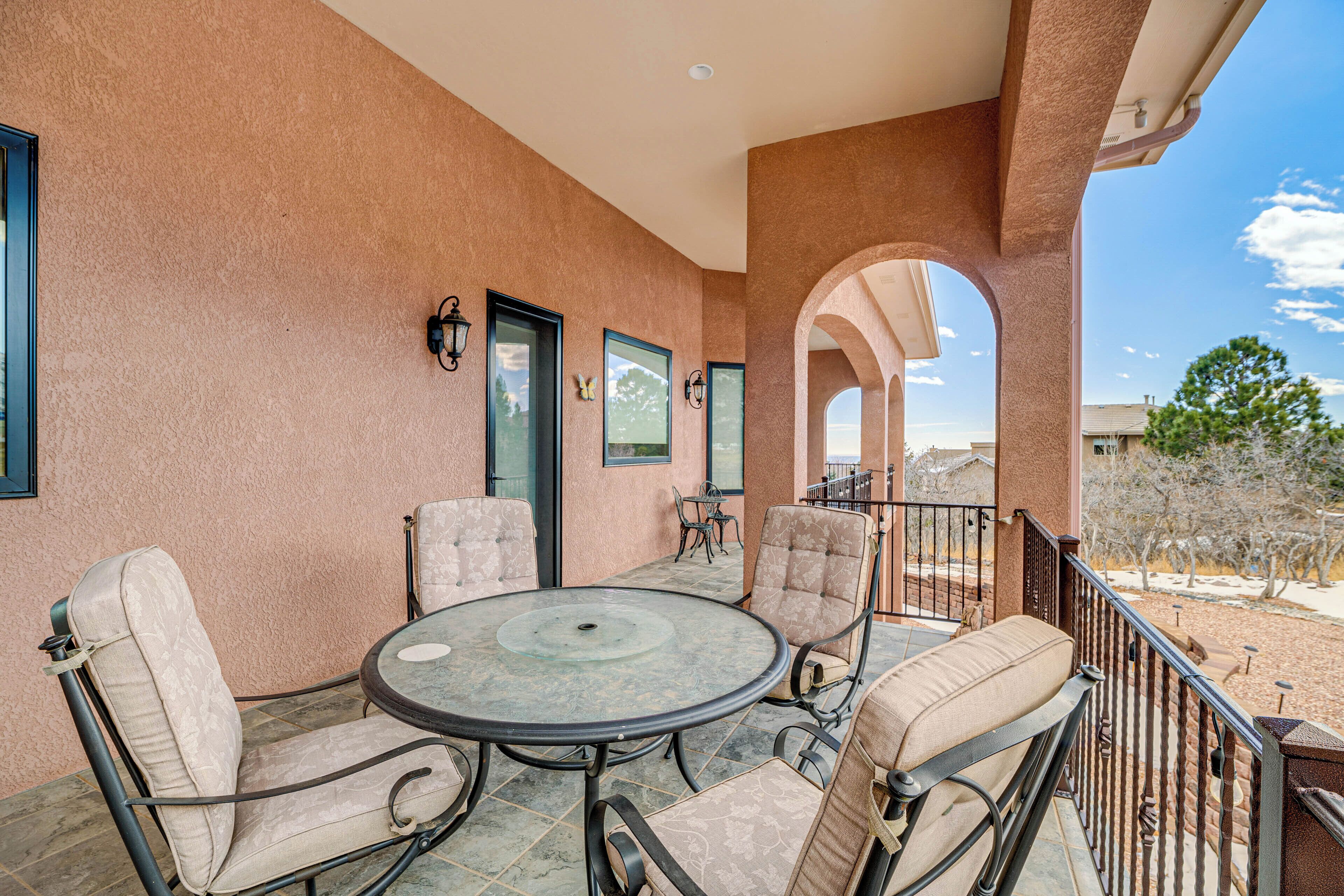 A covered patio area with a round table and four cushioned chairs, a door, and a view of the surrounding landscape.