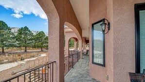 A balcony with stone flooring, a metal railing, and a view of a landscaped area with trees and a building in the background. - Colorado Springs Home ~ 4 Mi to Garden of the Gods (Colorado Springs)