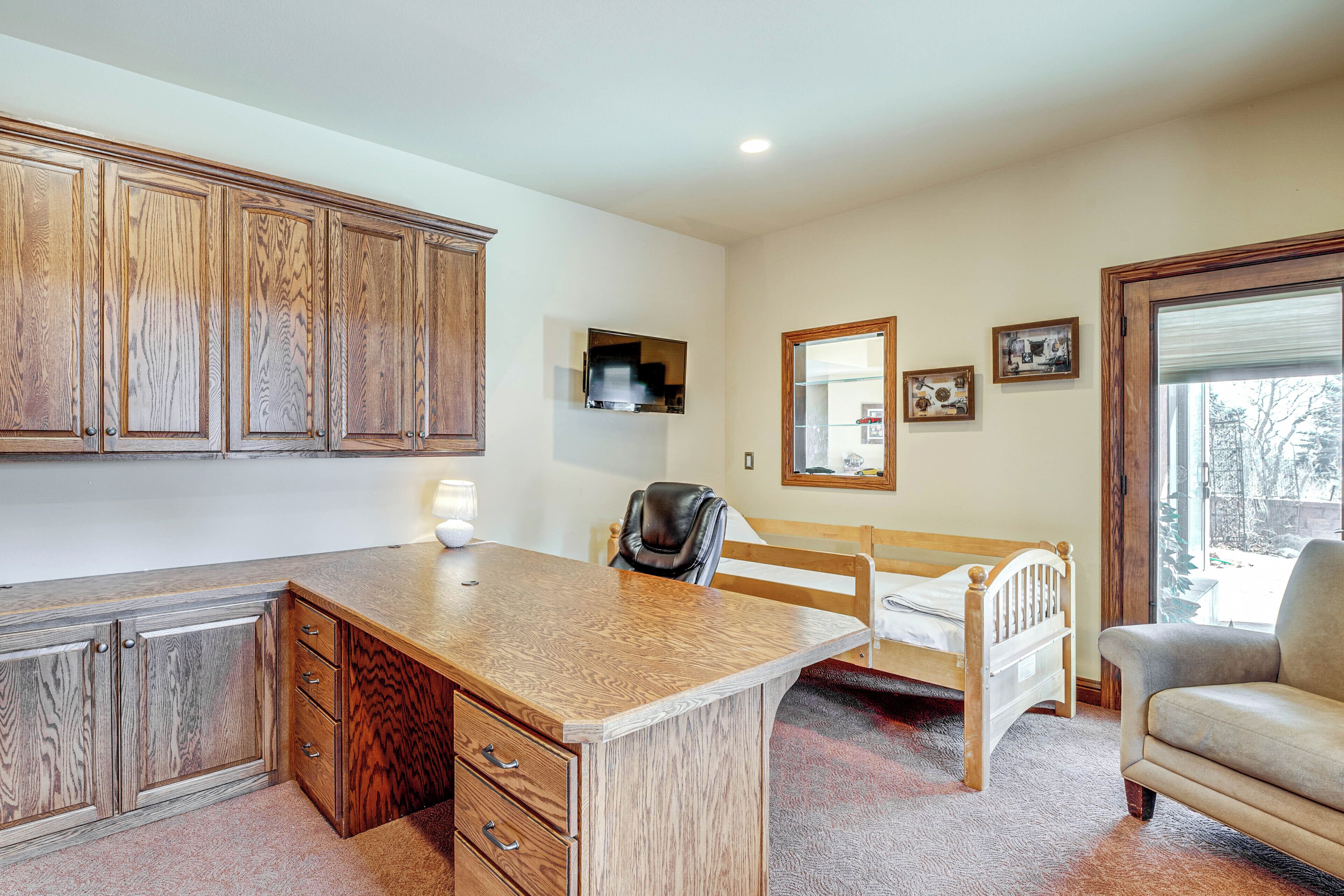 Een kamer met een houten bureau, een bed, een stoel en een raam met uitzicht.