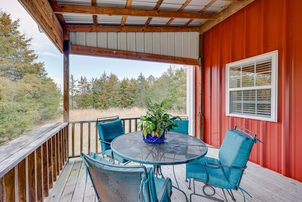 Relax in this serene outdoor seating area with a round table and four chairs, surrounded by a wooded landscape.