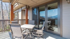 A covered patio with a table and chairs, a sliding glass door leading to a dining area, and a view of mountains. - Chalakee Lodge CA-3- Mountain View, Gated Resort, Indoor/Outdoor Pools & Hot Tub (Boone)