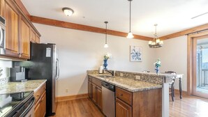 A kitchen with wooden cabinets, granite countertops, a built-in dishwasher, and pendant lighting. - Chalakee Lodge CA-3- Mountain View, Gated Resort, Indoor/Outdoor Pools & Hot Tub (Boone)