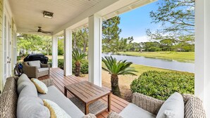 Une véranda aménagée avec des meubles en osier, une table en bois et une vue sur un lac et un terrain de golf.
