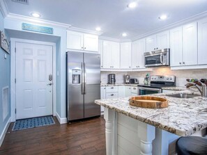 A modern kitchen with white cabinets, stainless steel appliances, a marble countertop, and a built-in oven.