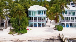 Une propriété située en bord de mer, avec un bâtiment principal entouré de palmiers, dotée de nombreux balcons et donnant sur une plage de sable.