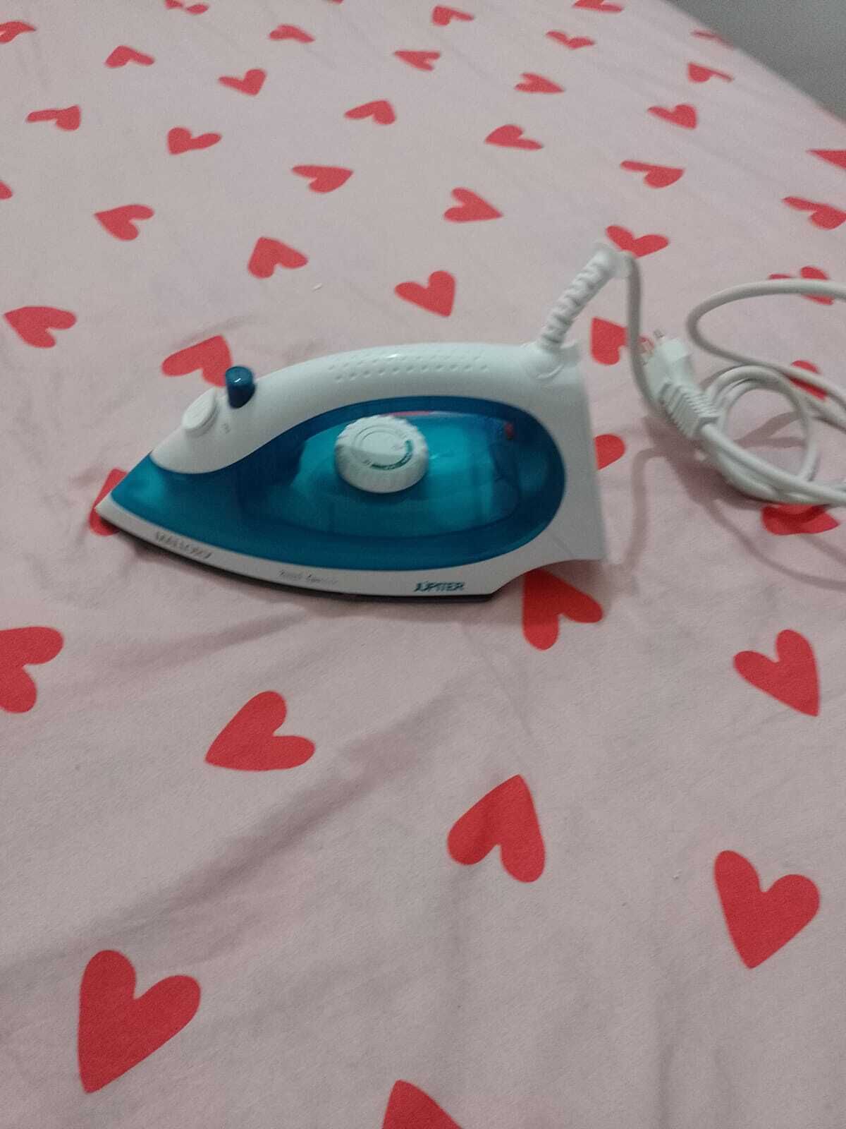 An iron on a bed with a heart pattern.